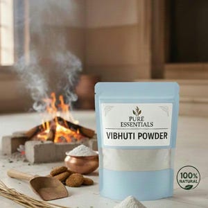 Könnte beinhalten: Ein hellblauer Beutel mit "Vibhuti Powder" von Pure Essentials, mit einem "100% Natural" Siegel. Ein kleiner Haufen Pulver und eine Kupferschale mit Pulver befinden sich im Vordergrund. Im Hintergrund brennt ein kleines Feuer.