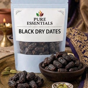 May include: A stand-up pouch labelled Pure Essentials Black Dry Dates containing dark, wrinkled dried dates. A dark brown bowl filled with dates, a small dish of green cardamom pods, and loose saffron threads sit on a gold-toned metal tray.