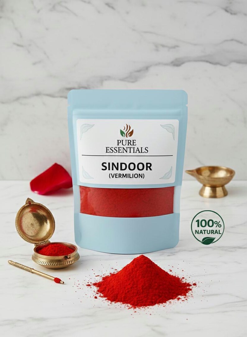 May include: A light blue pouch labeled "PURE ESSENTIALS" containing red sindoor (vermilion) powder. A small pile of the red powder sits in front of the pouch. A small, open, gold-colored container with a red powder is to the left.