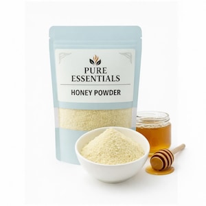 May include: A light blue pouch labeled "PURE ESSENTIALS HONEY POWDER" next to a white bowl filled with honey powder. A small jar of honey and a wooden honey dipper are also present, with honey dripping from the dipper.