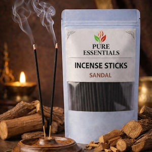 Op de afbeelding: Een pakket wierookstokjes van "Pure Essentials" met de geur "Sandelhout". Twee brandende wierookstokjes produceren rook en staan in een houten houder. De achtergrond bevat stukken hout en een brandende kaars.