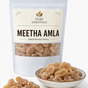 Puede incluir: Una bolsa blanca vertical etiquetada como Pure Essentials Meetha Amla Sweetened Amla que contiene trozos de fruta seca de color ámbar. Un pequeño cuenco de cerámica lleno de la misma fruta translúcida azucarada se sitúa delante, con varios trozos esparcidos.