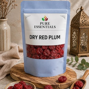 May include: A light blue stand-up pouch labelled Pure Essentials Dry Red Plum containing dried red plums. The pouch features a clear window displaying the contents. Several dried red plums are scattered on the surface, with some in a small bowl and a wooden scoop.
