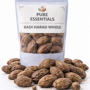 May include: A clear pouch labeled "PURE ESSENTIALS" containing "BADI HARAD WHOLE" brown, oval-shaped seeds. Some seeds are scattered around the base of the pouch. The seeds have a textured surface and are a dark brown color.