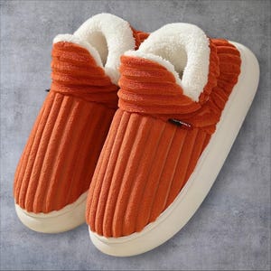 May include: A pair of orange corduroy slippers featuring a high-top design with a thick white fleece lining and a chunky white rubber sole. A small black and red tag with the word SPORT is visible on the side of the right slipper.