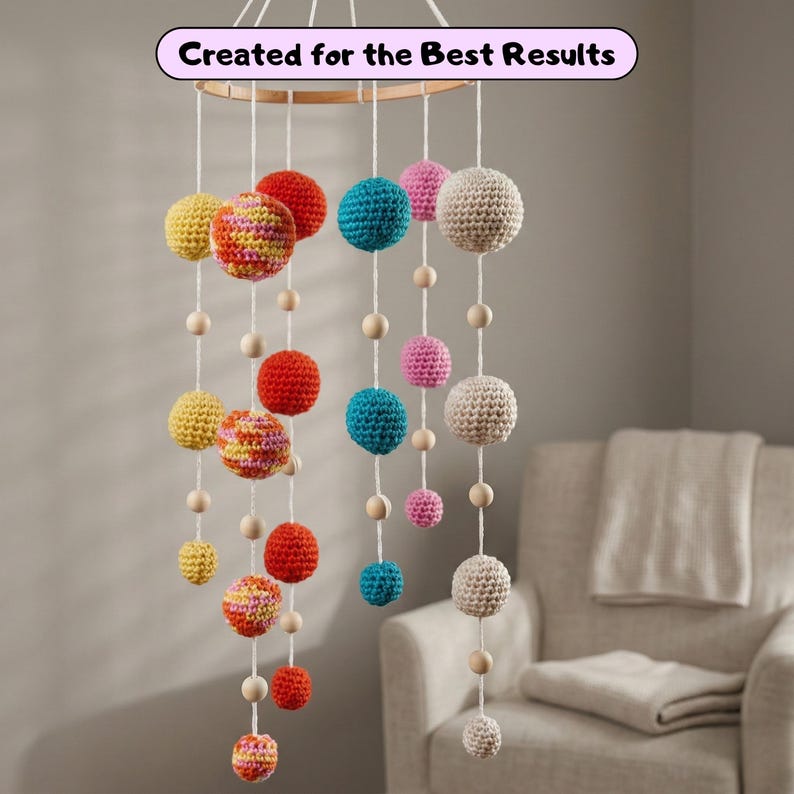 May include: A colorful, handmade mobile featuring crocheted spheres in various sizes and colors, including red, yellow, pink, blue, and cream. The spheres are suspended from a wooden ring with wooden beads and white string. Text reads "Created for the Best Results."