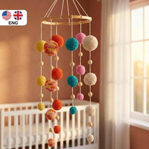 May include: A colorful baby mobile with a wooden ring and hanging crochet spheres in various colors, including yellow, orange, teal, pink, and cream. Wooden beads are interspersed along the strings. The mobile hangs above a white crib.
