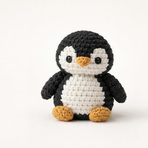 May include: A handmade crochet penguin doll. The penguin has a black head, wings, and back, a white belly, and orange feet and beak. The doll is made with a tight stitch pattern, giving it a textured appearance. The penguin is sitting upright.