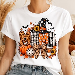 Puede incluir: Una camiseta blanca con un estampado gráfico de la palabra MAMA en varios patrones, incluyendo estampado de leopardo, cuadros blancos y negros, naranja con flores blancas y rayas blancas y negras. Incluye un sombrero de bruja, calabazas y un lazo.