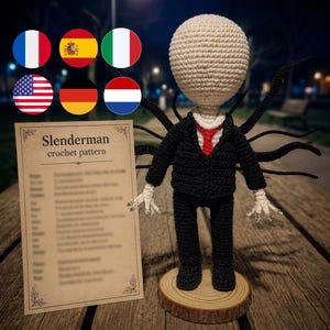 May include: A crocheted Slenderman doll with a pale round head, wearing a black suit with a red tie, standing on a circular wooden base. Multiple black tentacles extend from the back. A card labeled Slenderman crochet pattern is visible.