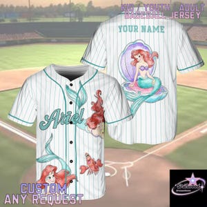 A personalized baseball jersey featuring the character Ariel from the Disney movie "The Little Mermaid". The jersey has a white background with stripes and illustrations of Ariel and other mermaid characters. The jersey is designed to be customized with a name and possibly other details.