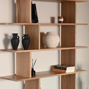 May include: A wooden bookcase in light tones, featuring various decorative objects: black vases, a textured vase, books, candles, and a speaker with the "Marshall" logo.