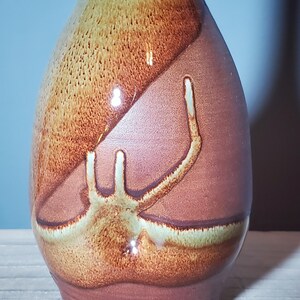 May include: A handcrafted ceramic vase with a unique design. The vase features a blend of brown, tan, and reddish-brown hues. The surface has a textured appearance with a distinctive abstract pattern in lighter tones.