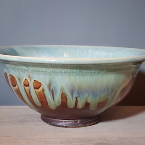 May include: A large, handcrafted ceramic bowl with a wide rim. The bowl features a blend of colours, including a light blue rim, a green and brown centre, and a dark brown base. The bowl is likely used for serving or display.