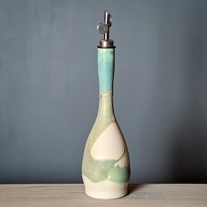 May include: A ceramic olive oil bottle with a green, blue, and white glaze. The bottle has a spout with a metal top.