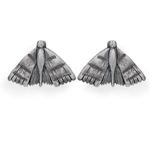May include: A pair of silver-toned moth-shaped earrings. Each earring features detailed wings with striped patterns and a small head. The earrings are designed to resemble moths, with intricate textures and a realistic appearance.