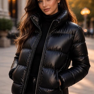 Puede incluir: Una chaqueta acolchada negra con cuello alto, cremallera frontal completa y paneles acolchados horizontales. La chaqueta presenta un acabado liso y ligeramente brillante, mangas largas y dos bolsillos laterales sobre un jersey de cuello alto.