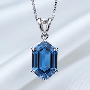 Op de afbeelding: Een zilveren ketting met een zeshoekige, diepblauwe edelsteen hanger. De hanger is facetgeslepen, vangt het licht en hangt aan een fijne ketting. De edelsteen is gezet in een zilveren montuur.