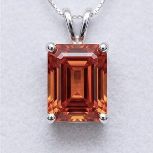 May include: A silver pendant necklace featuring a rectangular, orange gemstone. The gemstone is set in a silver bezel with four small silver prongs. The chain is a delicate silver box chain.