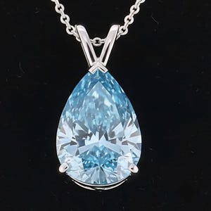 Könnte beinhalten: Ein tropfenförmiger, hellblauer Edelsteinanhänger an einer Silberkette. Der Edelstein ist facettiert und reflektiert das Licht. Der Anhänger ist in einer silbernen Metalleinfassung gefasst.