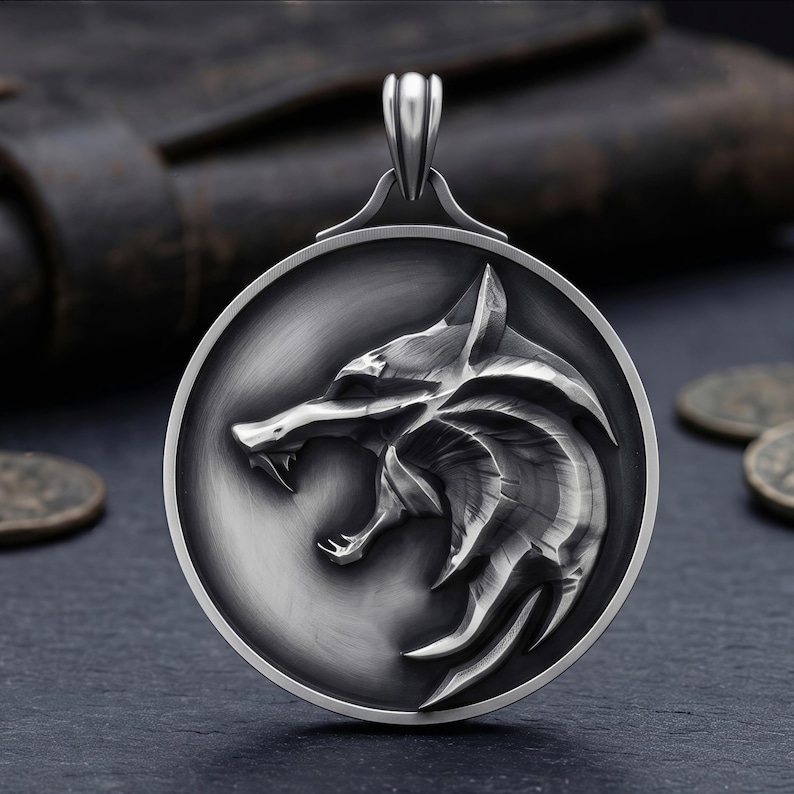 May include: A silver pendant with a detailed wolf head design inside a circular frame. The wolf is shown with its mouth open, teeth bared. The pendant has a bail for a chain and is set against a dark backdrop.
