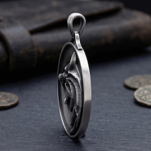 May include: A silver pendant featuring a detailed wolf head design. The oval-shaped pendant has a loop for a chain. The wolf's head is in profile, with intricate detailing on the fur and features. The pendant is displayed on a dark surface.