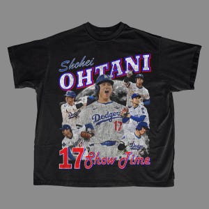 May include: Black t-shirt featuring a graphic of Shohei Ohtani in a Dodgers uniform. The design includes the text "Shohei Ohtani" in blue and red, along with "17 Show Time". The shirt showcases multiple images of the baseball player.