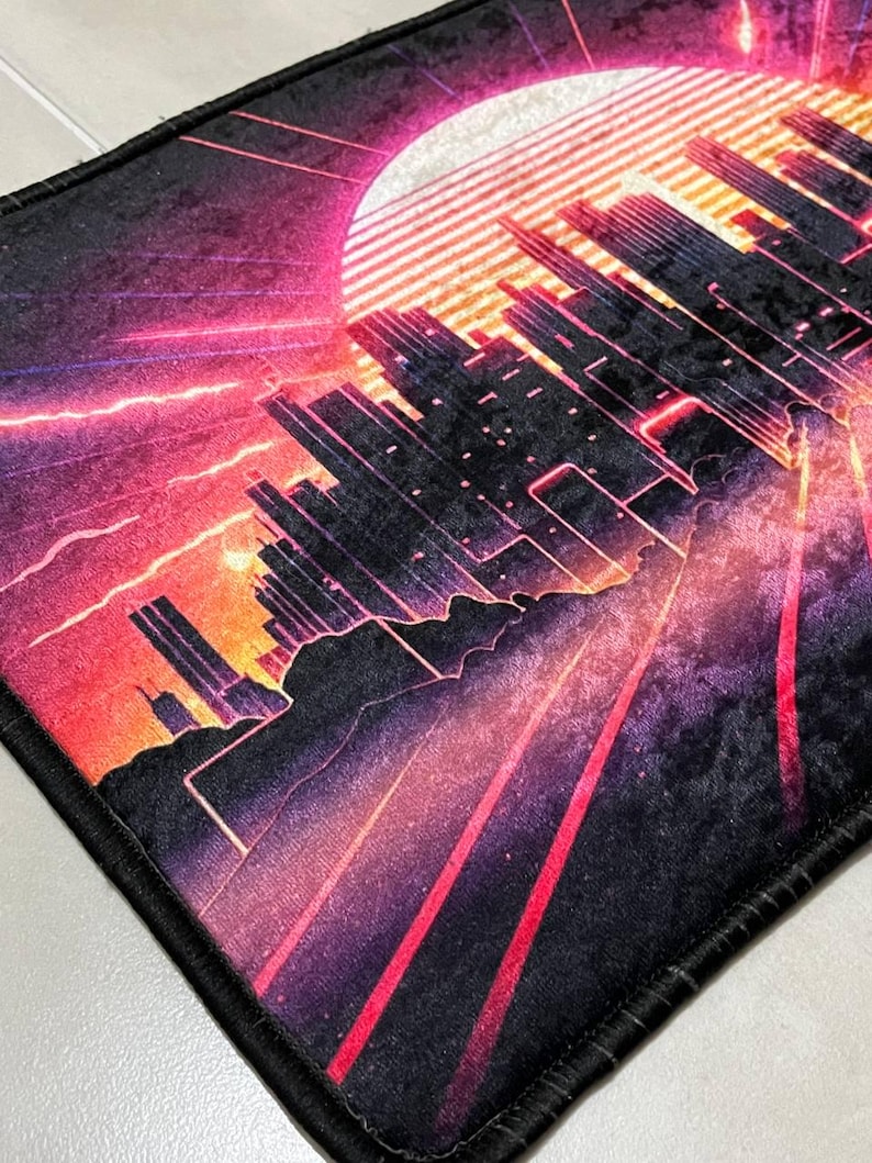 Puede incluir: Alfombra rectangular con un dise&ntilde;o de paisaje urbano retro. La obra de arte presenta un gran sol, rascacielos y l&iacute;neas radiantes en tonos rojos, morados y naranjas. La alfombra tiene un borde negro. El dise&ntilde;o evoca una ciudad futurista.