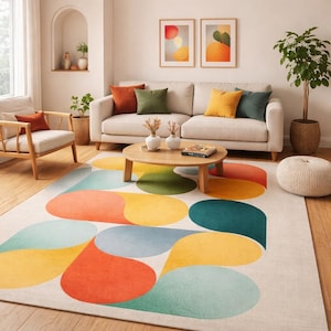 Può includere: Un soggiorno con un divano color crema con cuscini colorati, un tavolino rotondo in legno e un tappeto fantasia. Il tappeto ha uno sfondo bianco e grandi forme a goccia colorate in arancione, giallo, verde e blu.