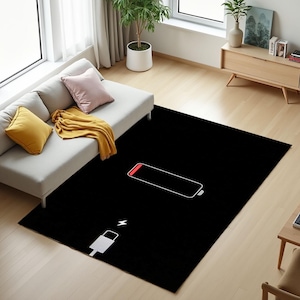 Puede incluir: Una alfombra rectangular negra con un contorno blanco de un s&iacute;mbolo de bater&iacute;a baja y una parte superior roja. Tambi&eacute;n hay un icono de cable de carga blanco. La alfombra est&aacute; sobre un suelo de madera clara, cerca de un sof&aacute; y una peque&ntilde;a mesa de madera.