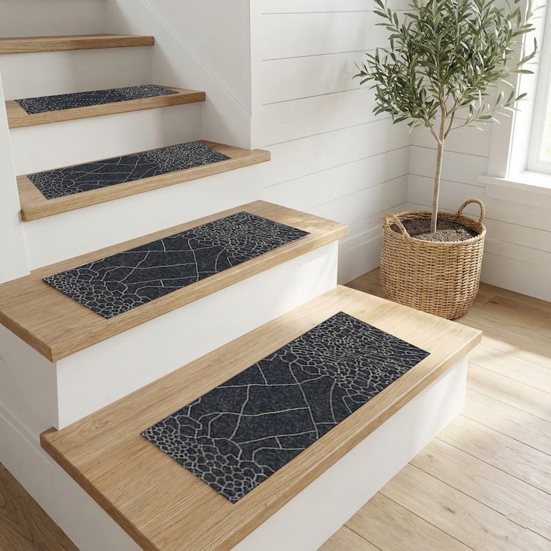 May include: Stair treads with a dark grey and white pattern are installed on wooden stairs. The treads have a geometric design. The stairs are in a well-lit room with a white wall and a potted plant.