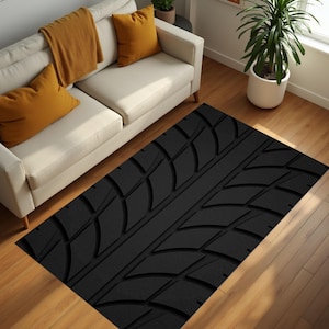 May include: A black rectangular rug featuring a tyre tread design. The rug is positioned on a wooden floor in front of a white sofa with yellow cushions and a mustard-coloured throw. A potted plant is also visible.