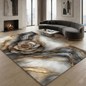 May include: A rectangular area rug with a large, stylized rose design. The rug features a blend of gray, white, and gold tones, creating a luxurious and artistic aesthetic. The rug is placed in a modern living room setting.