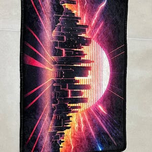 Puede incluir: Alfombra rectangular negra con un dise&ntilde;o retro de paisaje urbano. La imagen presenta una silueta de ciudad estilizada sobre un fondo vibrante de tonos rojos, naranjas y morados, con un gran sol y rel&aacute;mpagos.