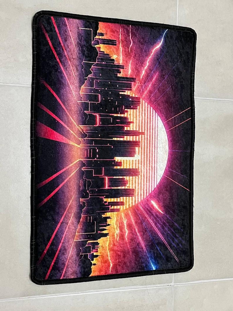 Puede incluir: Alfombra rectangular negra con un dise&ntilde;o retro de paisaje urbano. La imagen presenta una silueta de ciudad estilizada sobre un fondo vibrante de tonos rojos, naranjas y morados, con un gran sol y rel&aacute;mpagos.