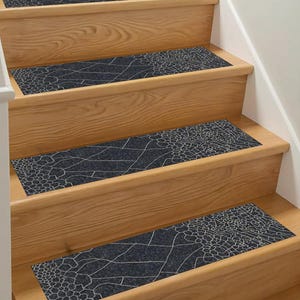 May include: Dark grey stair treads with a white, geometric pattern, installed on wooden stairs. The treads provide a decorative and functional element for home decor, with each tread measuring approximately 70 cm in length.