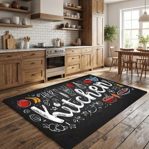 May include: Black rectangular kitchen rug with white script and illustrations of kitchen utensils and food items. The word "Kitchen" is prominently displayed. The rug is on a wooden floor in a kitchen setting.
