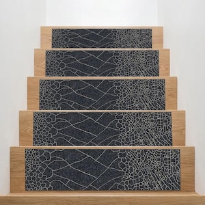 May include: Stair treads featuring a dark grey, textured pattern with light-coloured lines. The treads are set into light-coloured wooden steps, creating a modern look. The pattern resembles a cracked surface, adding a stylish touch to the home.