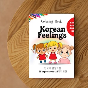 May include: A coloring book titled "Korean Feelings" with illustrations of three cartoon girls expressing different emotions. The cover includes text in English and Korean, with a red accent and a wooden table background.