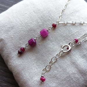 May include: A silver chain necklace with a pink gemstone pendant. The pendant has three pink gemstones, one large square and two smaller round ones.