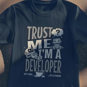 May include: Dark blue t-shirt featuring the white text "TRUST ME I'M A DEVELOPER". The design includes cartoon robots and a coffee cup. Below the text are the words "NOT A BUG... IT'S A FEATURE".