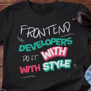 Könnte beinhalten: Schwarzes T-Shirt mit dem Text "FRONTEND DEVELOPERS DO IT WITH STYLE" in Weiß, Türkis und Pink. Eine Sonnenbrille liegt auf dem Shirt. Das Shirt liegt auf einer Holzoberfläche.