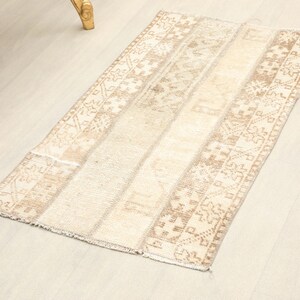 May include: A rectangular area rug featuring a neutral color palette of beige, cream, and light brown. The rug displays a series of vertical bands with intricate geometric patterns and cross-like motifs, finished with a short fringe on the ends.