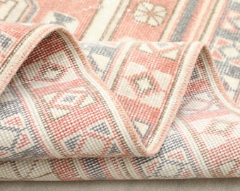Könnte beinhalten: Nahaufnahme eines gefalteten Teppichs im Vintage-Stil mit geometrischem Muster. Der Teppich hat eine Farbpalette aus Rot, Creme und Grau. Das Design umfasst Diamant- und Blumenmotive.