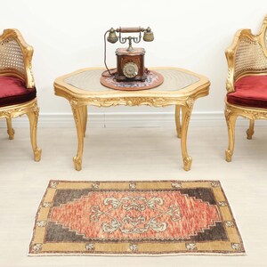 May include: An antique living room scene featuring two ornate gold chairs with red cushions, a gold table with a vintage telephone, and a small, rectangular rug with a red and brown pattern.