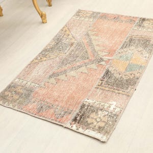 May include: A rectangular area rug featuring a patchwork design composed of various textile segments. The rug displays a muted color palette of faded peach, charcoal gray, beige, and soft green, with geometric patterns and floral motifs throughout.