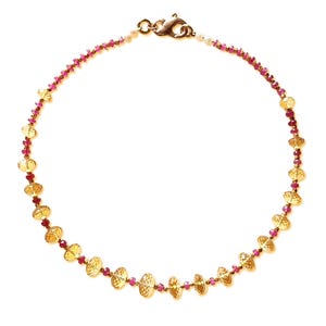 Op de afbeelding: Een goudkleurige ketting met getextureerde, ovale hangers en kleine, rode kralen. De ketting heeft een fijne ketting en een sluiting. Het ontwerp is symmetrisch, met de hangers gelijkmatig verdeeld over de ketting. Lengte: ongeveer 40 cm.