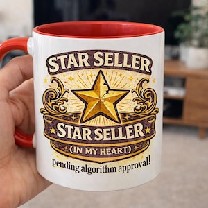 Op de afbeelding: Witte keramische mok met een rode binnenkant en handvat. De mok heeft de tekst "STAR SELLER" boven en onder een gouden sterontwerp. Extra tekst luidt "(IN MY HEART) pending algorithm approval!"