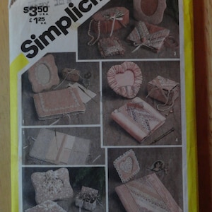 May include: Simplicity sewing pattern number 5296 for making a variety of small boxes and pouches. The pattern includes instructions for making a heart-shaped box, a round box, a rectangular box, and a pouch. The pattern is printed on a white background with yellow text and images.