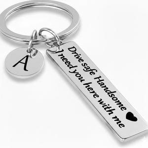May include: Silver keyring with a rectangular tag and a round charm. The rectangular tag has the text "Drive safe Handsome I need you here with me" and a heart symbol. The round charm has the letter "A".
